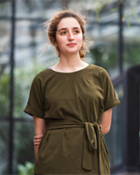 Teresa Homsi in a brown dress standing in front of a blurred out background.