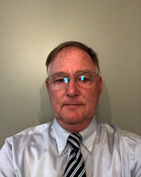 William Henderson in a light colored shirt and striped tie against a beige backdrop looking at the camera