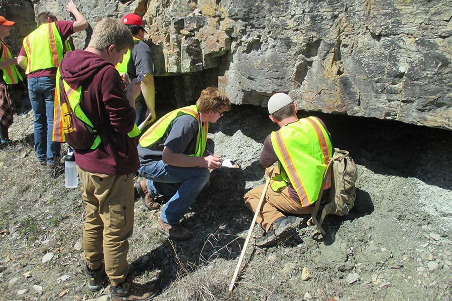 A group of people in yellow vests look under a large rock formation.