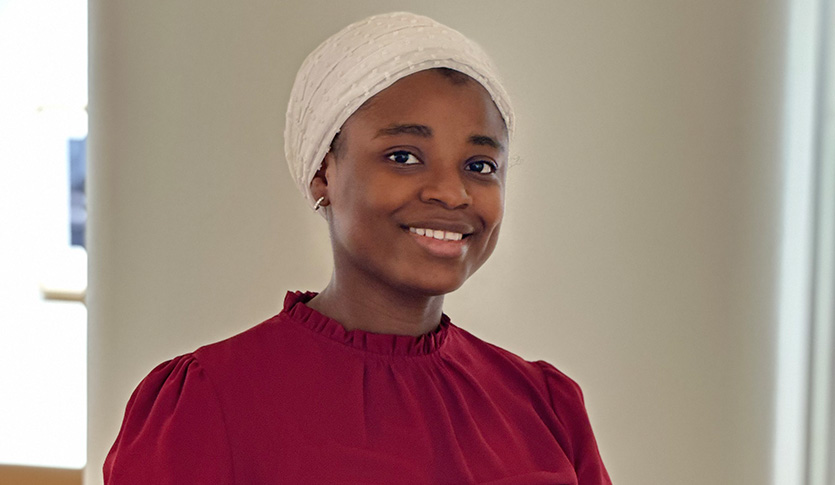Aminat Gbadamosi wearing a red shirt and white hat smiling at the camera.