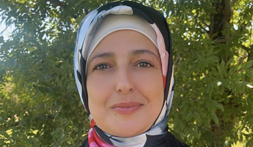 Muna Al-Kasasbeh in a head scarf outdoors in front of a tree smiling at the camera.