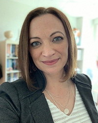 A woman in a dark jacket and striped blouse taking a selfie.