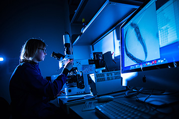 A female BioTechnology student examining a specimen under a microscope.
