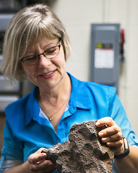 Mona Sirbescu in a blue shirt examining a rock on a lab table.