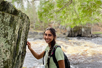 A woman with long dark hair in a braid standing in front of a river smiling at the camera.