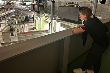 A student leaning on a railing overlooking racks of electronic equipment.