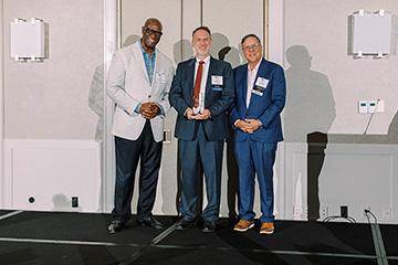 Three men standing on a stage with Dr. David Ford, holding an award, in the center.
