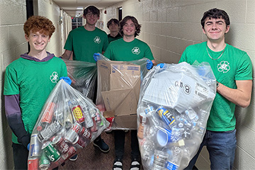 Students wearing green t-shirts holding bags of items to be recycled.