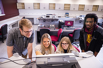 Four students examining a read out on a screen on a piece of equipment.