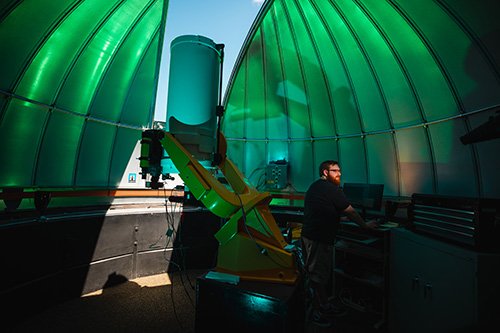 A man standing in the Brooks Astronomical Observatory setting coordinates in a computer for the telescope.