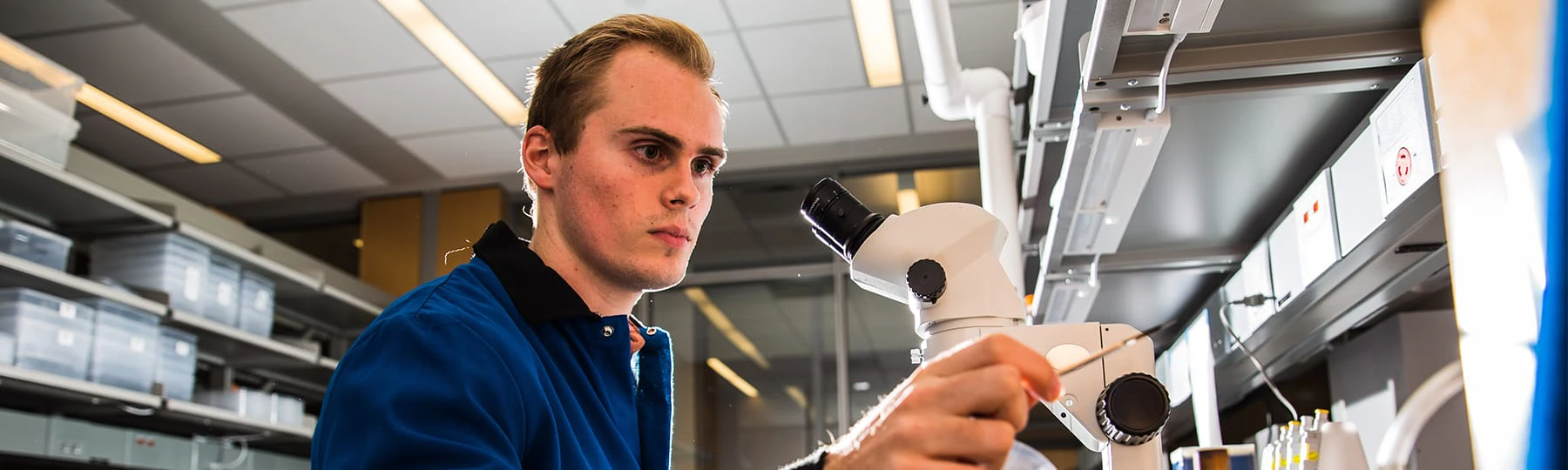 A student wearing a lab coat adjusts a microscope while working in a lab on campus.