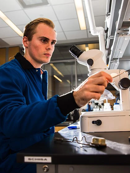 A student wearing a lab coat adjusts a microscope while working in a lab on campus.