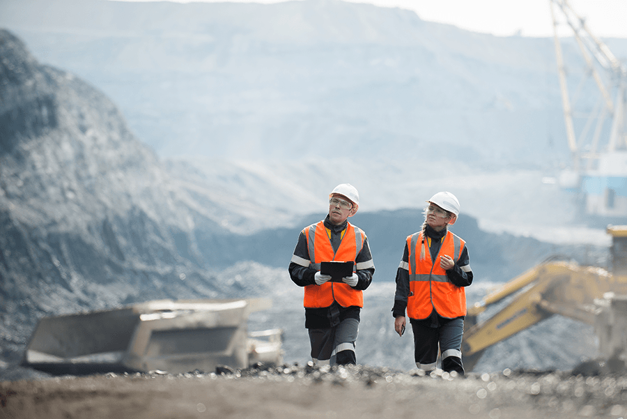 Two people in hard hats and vests walk through a quarry.