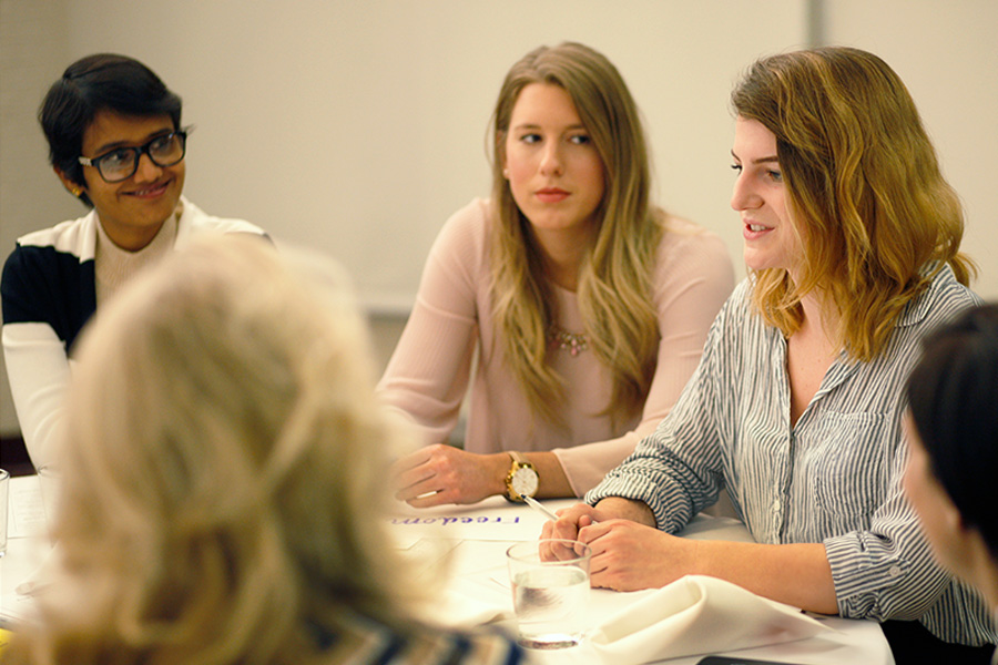 Five women at a table talking at an event.