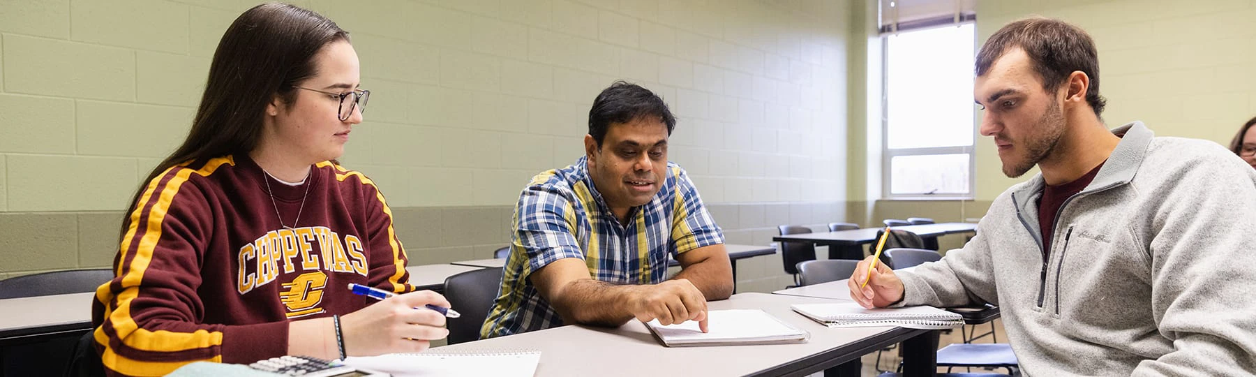 A female student in a Central Michigan University sweatshirt works with a faculty member in a button up and a male student in a grey zip up sweatshirt.