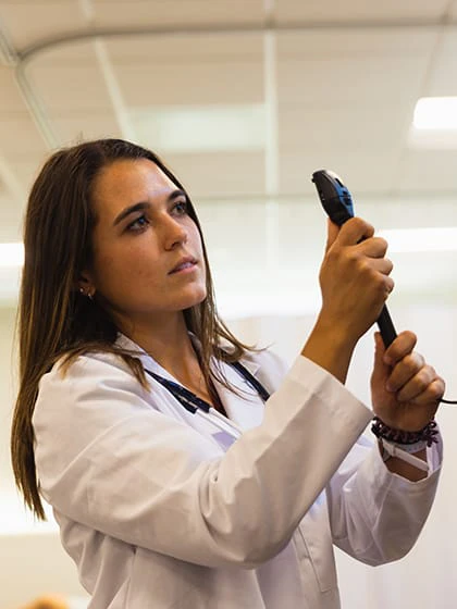 A pre-optometry student holds an instrument used to look at the eye up to a male patient.