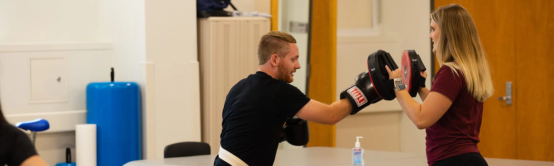 A pre-physical therapy student works with a patient to build strength through boxing work with pads.