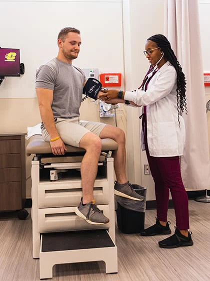 A pre-physician assistant student uses a blood pressure cuff and stethoscope to take a the blood pressure of a male patient.