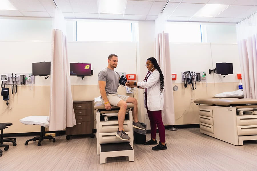 A pre-physician assistant student uses a blood pressure cuff and stethoscope to take a the blood pressure of a male patient.