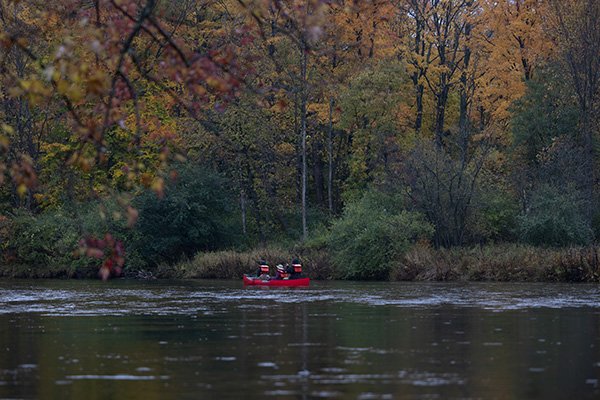 Three student in life jackets in a canoe paddling down a river in the fall.