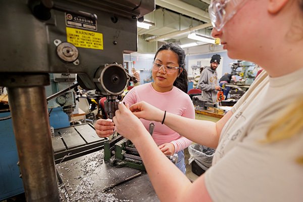 Two students using a drill press in the product design lab.