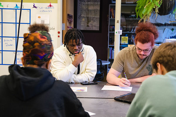 Four students sitting around a table with papers in front of them collaborating on a project.