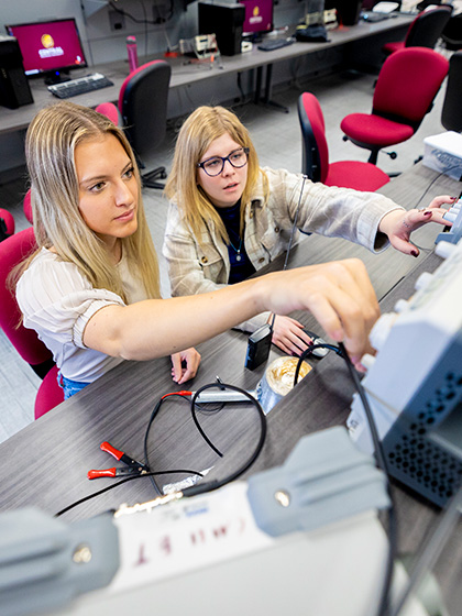 2 students adjusting knobs on an electronic device.