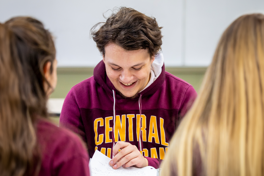 A student smiling at an assignment with two girls on the left and right.