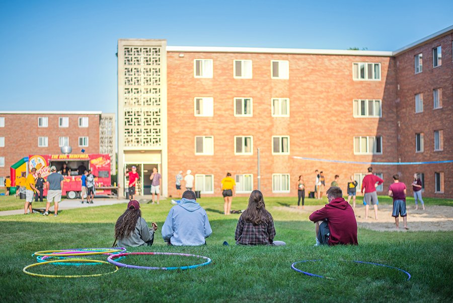 Students are outside of Emmons Hall playing volleyball, sitting on the grass and ordering food from a food truck.