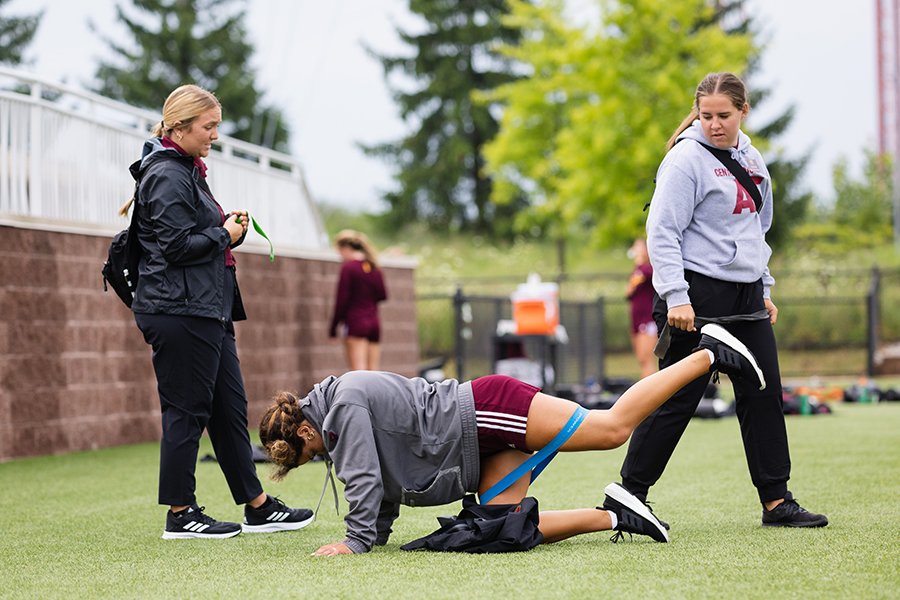 Two athletic training students working with a female soccer player during a practice