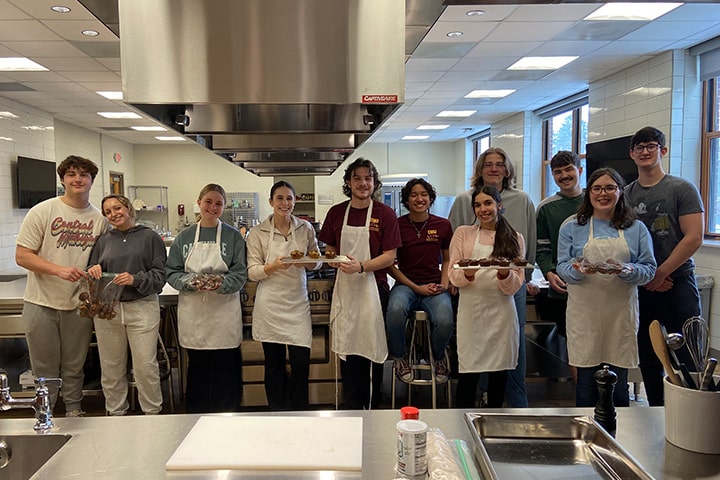 Eleven students pose together in front of a table in the test kitchen on campus.