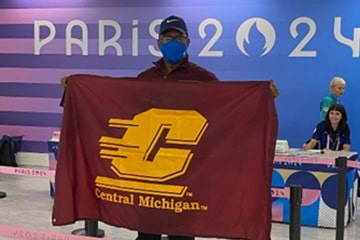 Dr. Vincent Mumford wearing a face mask poses holding a Central Michigan University flag.