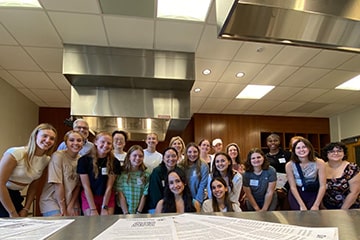 Students and faculty pose together in front of a table in the test kitchen on campus.