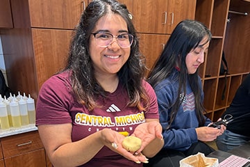 A student poses with a pressed piece of dough in her hands in the test kitchen on campus.