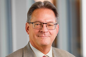 Professional headshot of Tom Masterson against a grey background.