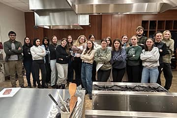 Students pose together in front of a cooking station in the test kitchen on campus.