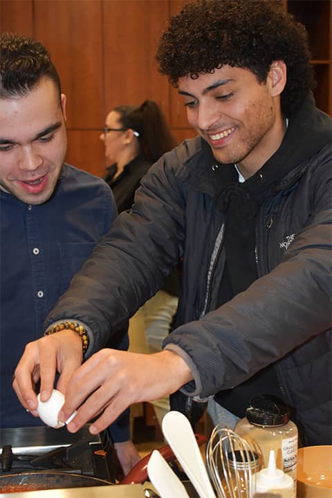 A student cracking an egg at a cooking station.