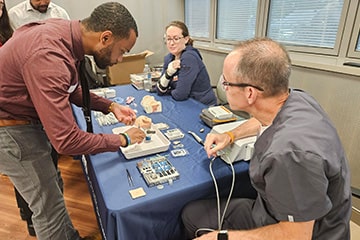 Audiology student practicing cochlear implant placement at a table with a group of people.