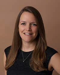 Professional headshot of Frances Wenzel in black attire against a brown background.