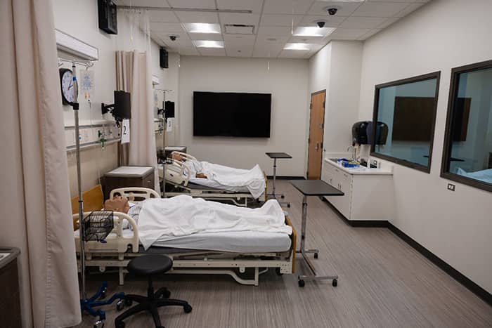 A high-fidelity health simulation room with two beds, two windows, and a television.