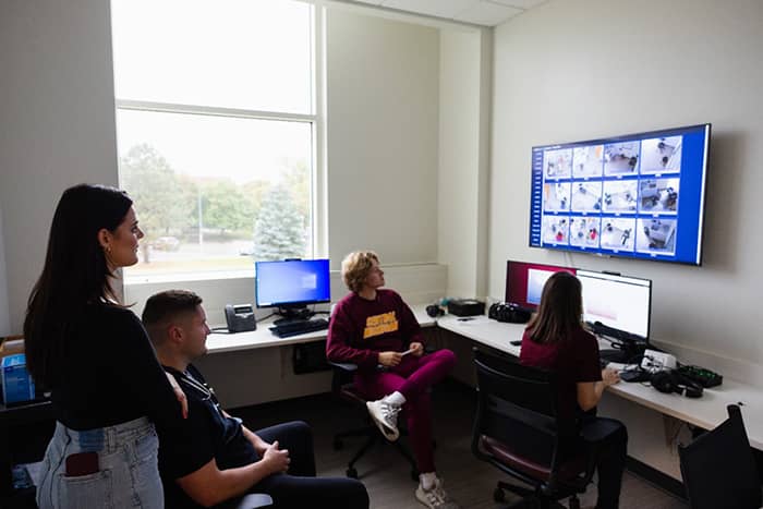 Four individuals watching live feeds on screens in the Interprofessional Education and Practice Center control room.