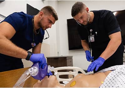 Two clinicians wearing blue gloves work on a mannequin.