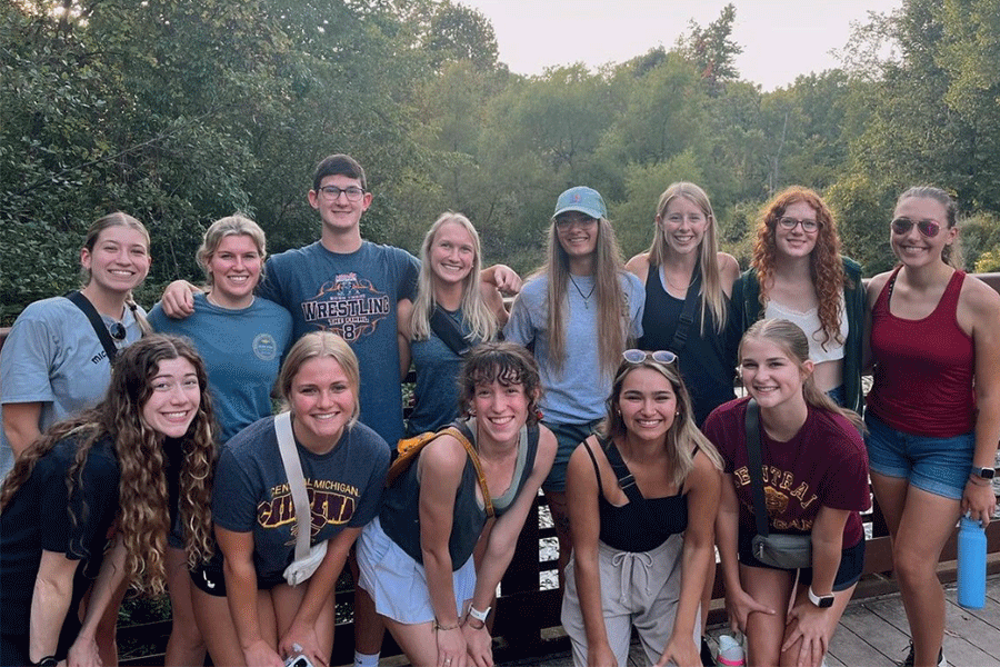 A group of students from the Pre-Physical Therapy club at Central Michigan University pose for a group photo outside. They are all standing on a bridge with trees and water behind them.