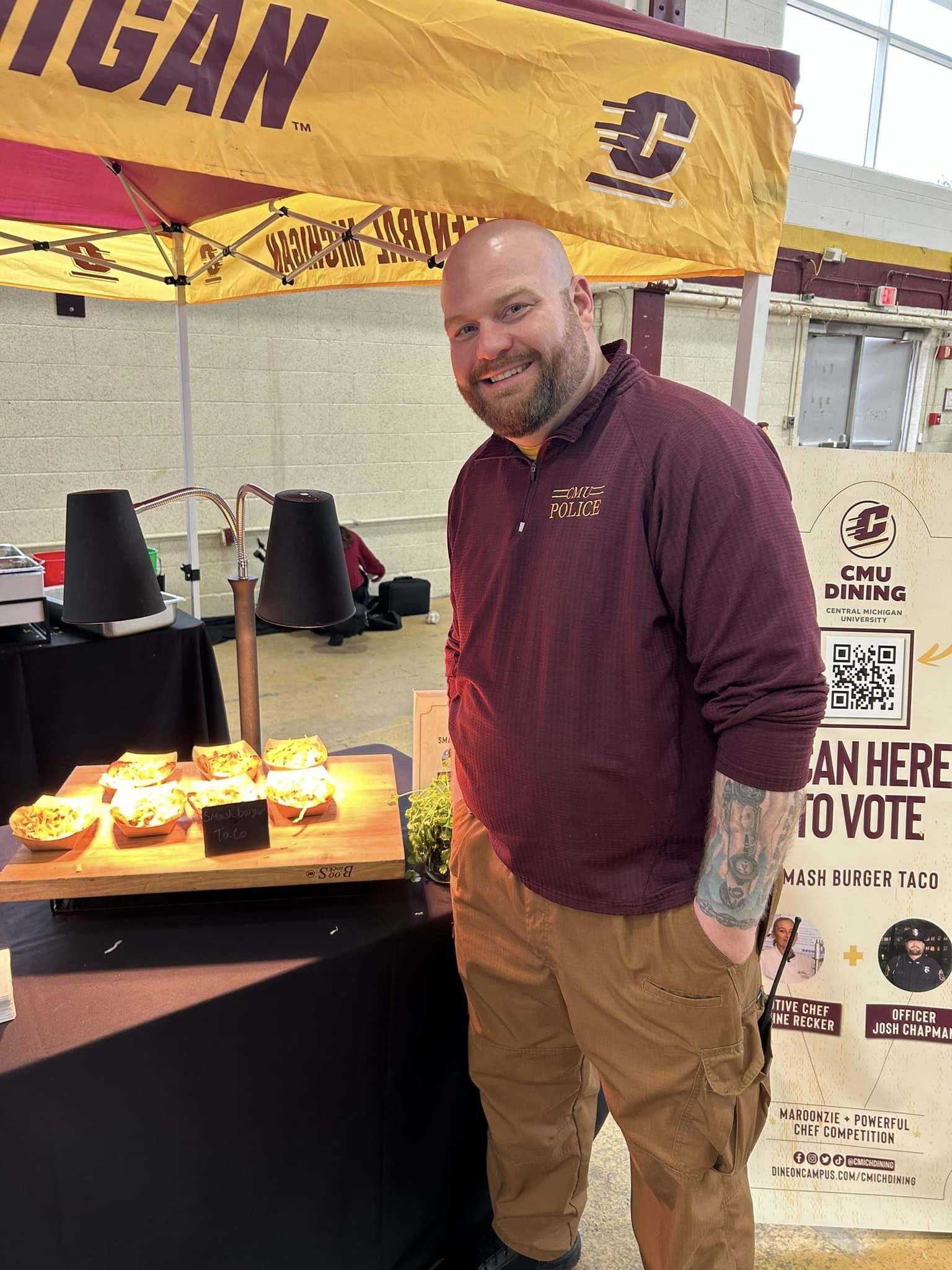 Officer Josh Chapman standing by his meal creation in collaboration with Chartwell. He is under a CMU tent with low lighting.