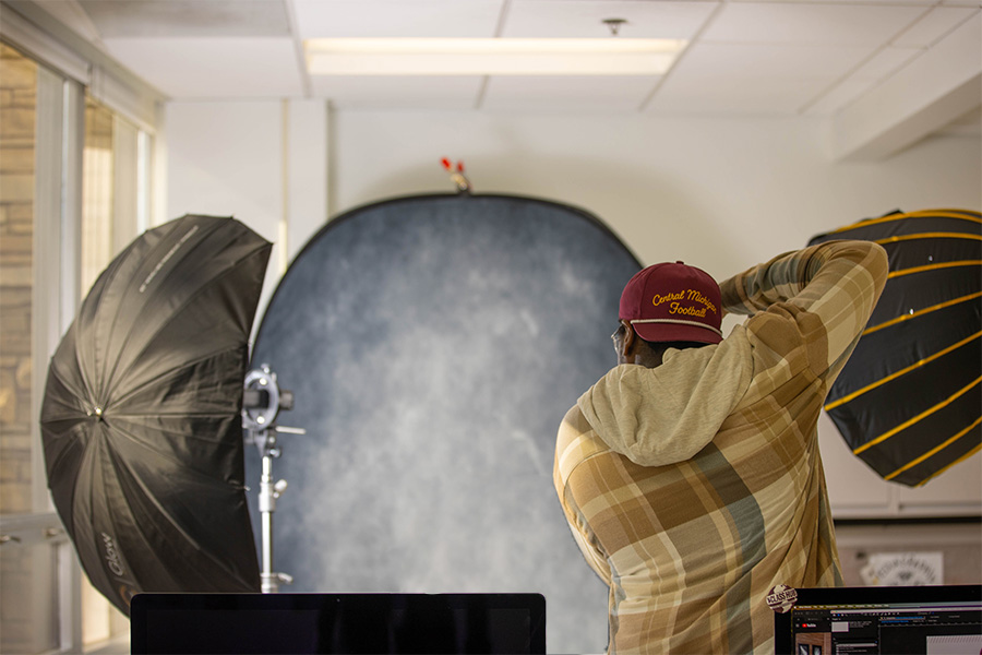 Student photographer taking professional portrait in studio with backdrop and lights.