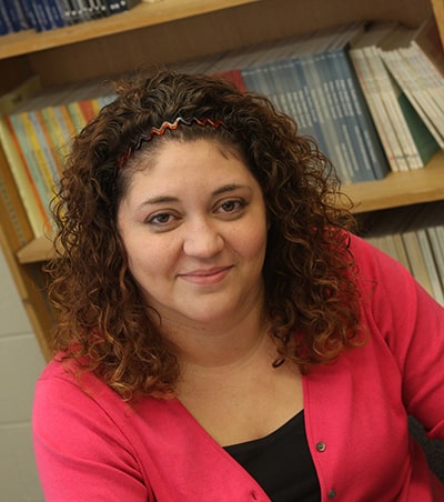 Dr. Cherie Strachan wears a black shirt and pink jacket while looking at the camera.