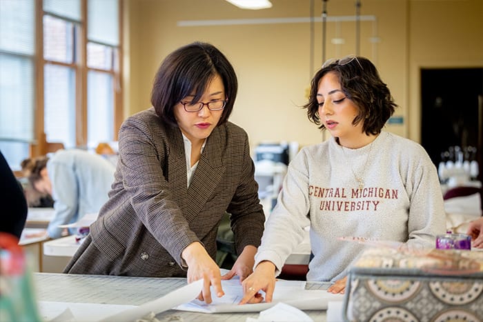 A faculty member works with a student in the fashion lab reviewing design plans.