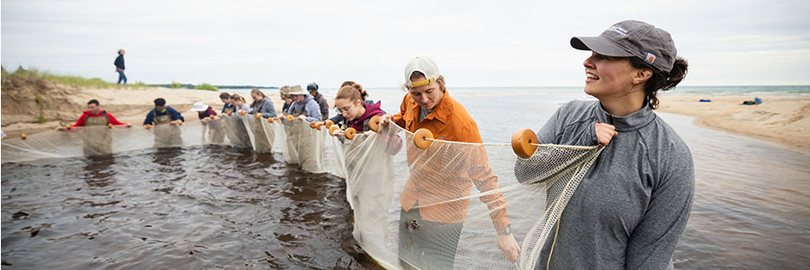 A group of people holding a long white net stand knee-deep in water.