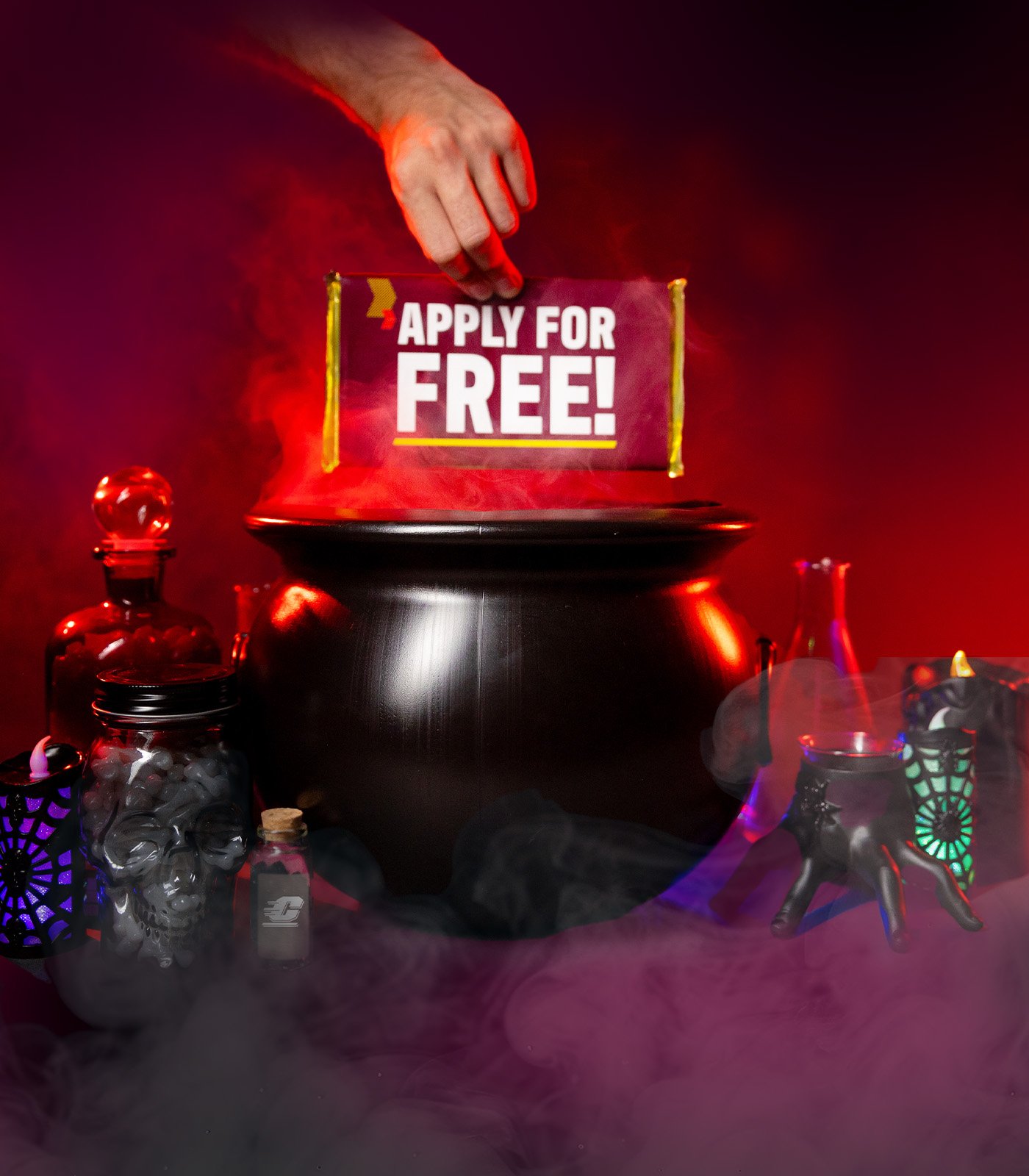 A spooky scene in dark maroon, reds and black with a black cauldron in the middle and a candy bar above it with "Apply for Free" on the wrapper.