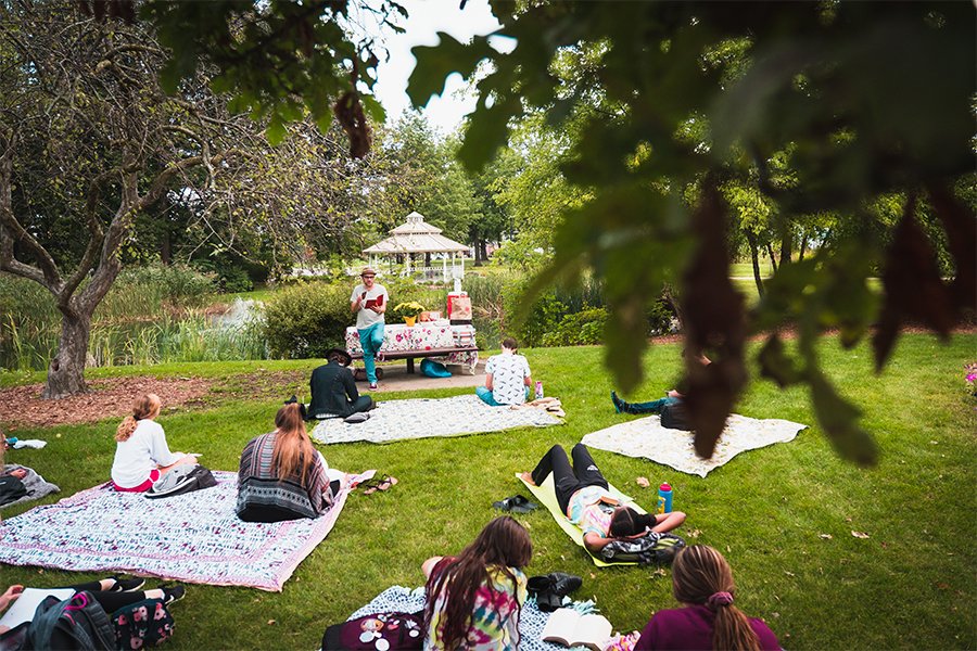 Students and faculty sit outside on picnic blankets and read aloud for English major lesson.